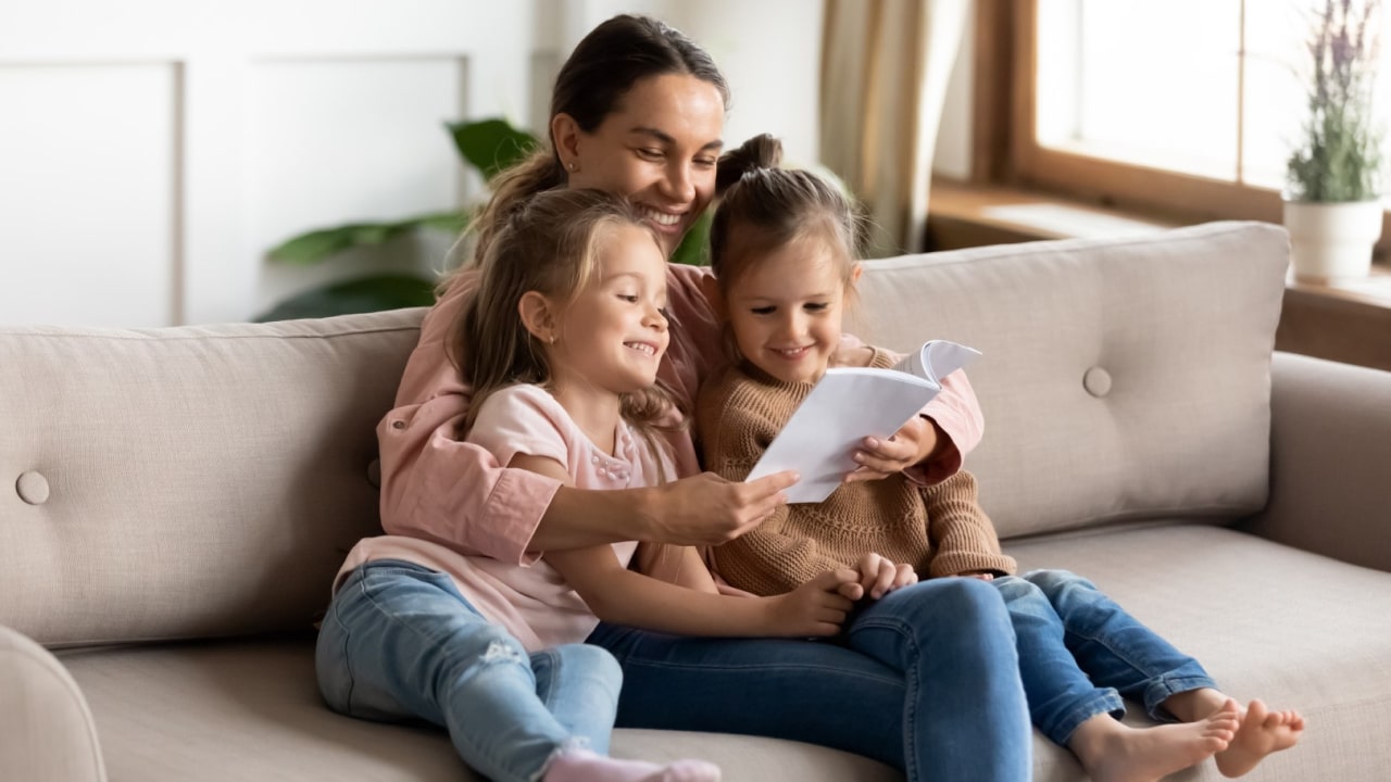 A mother and two young girls reading on a couch