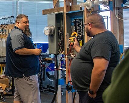 Ting employees using an electrical meter to read a panel